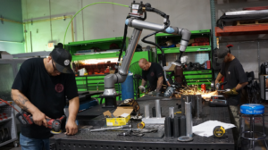 Robotic welding arm and metal fabricators working on custom metal fabrication project.