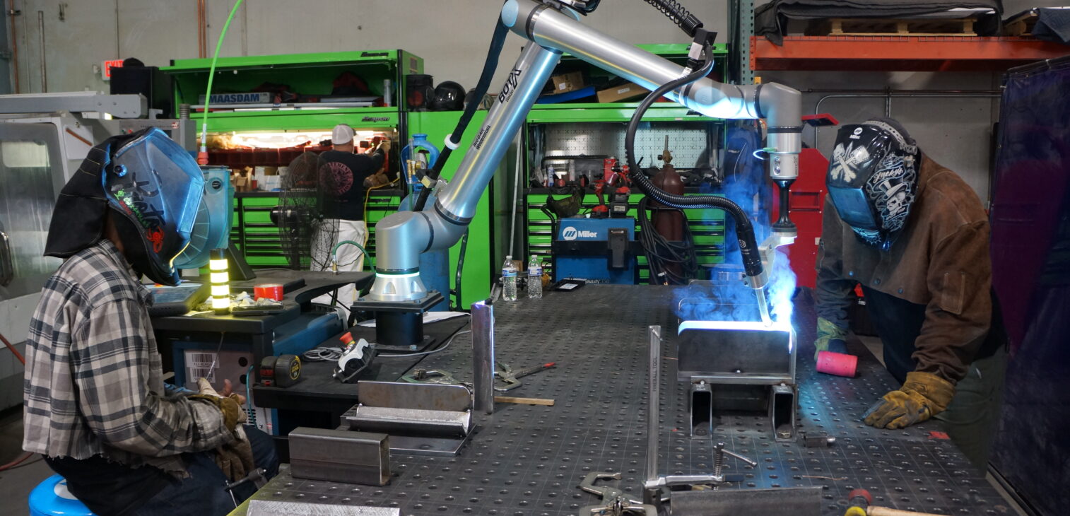 Robotic arm and skilled welders collaborating on metal fabrication project.
